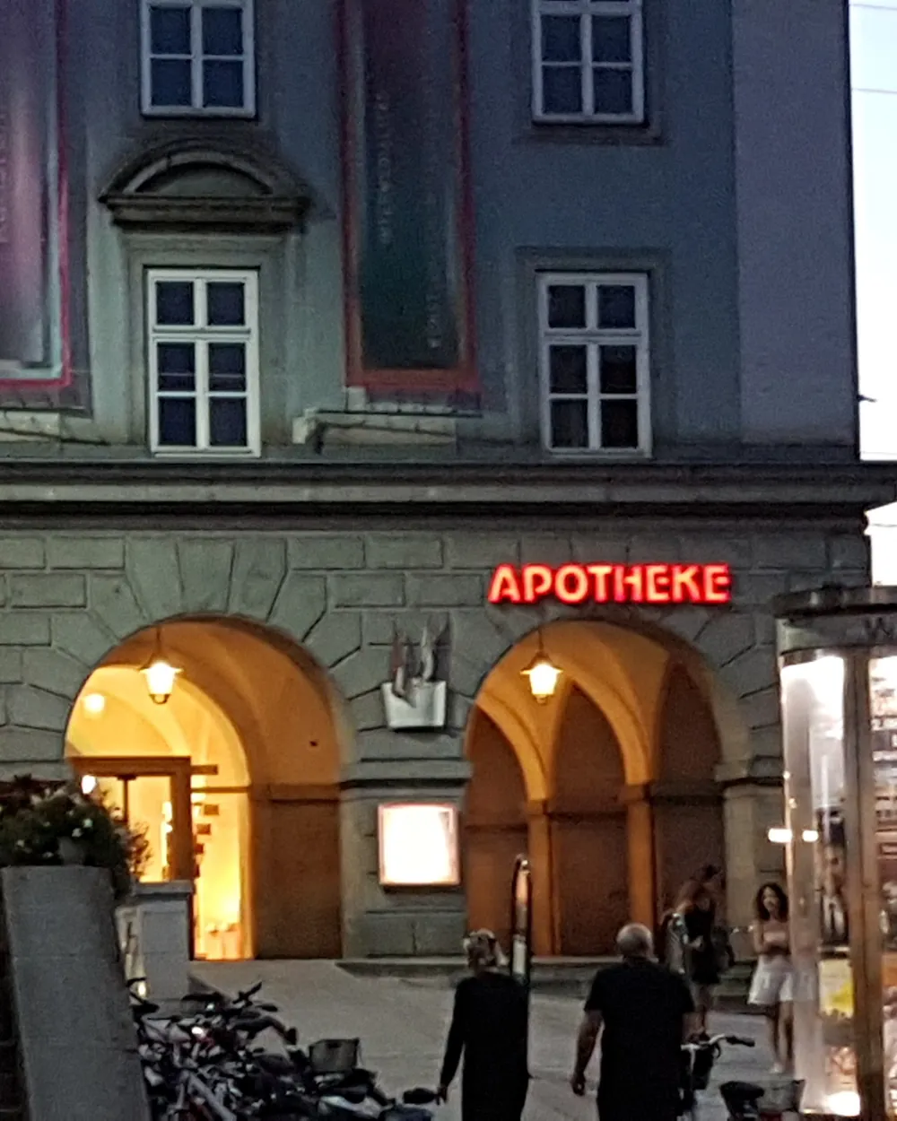 Roter Leuchtschriftzug „Apotheke“ über einem beleuchteten Arkadenbogen am Abend