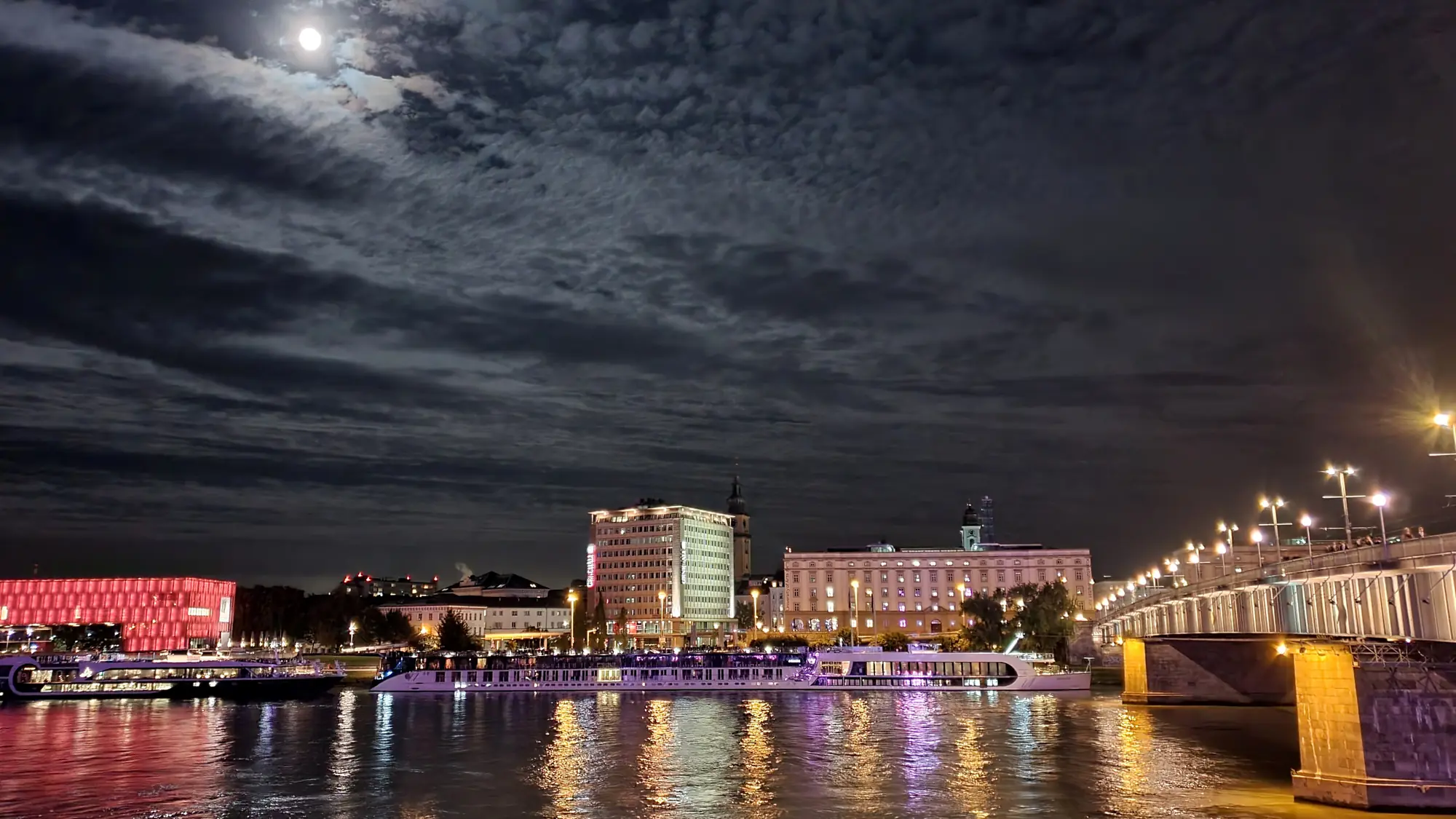 Nächtlicher Blick über die Donau auf das beleuchtete Linzer Südufer und die Nibelungenbrücke bei Vollmond