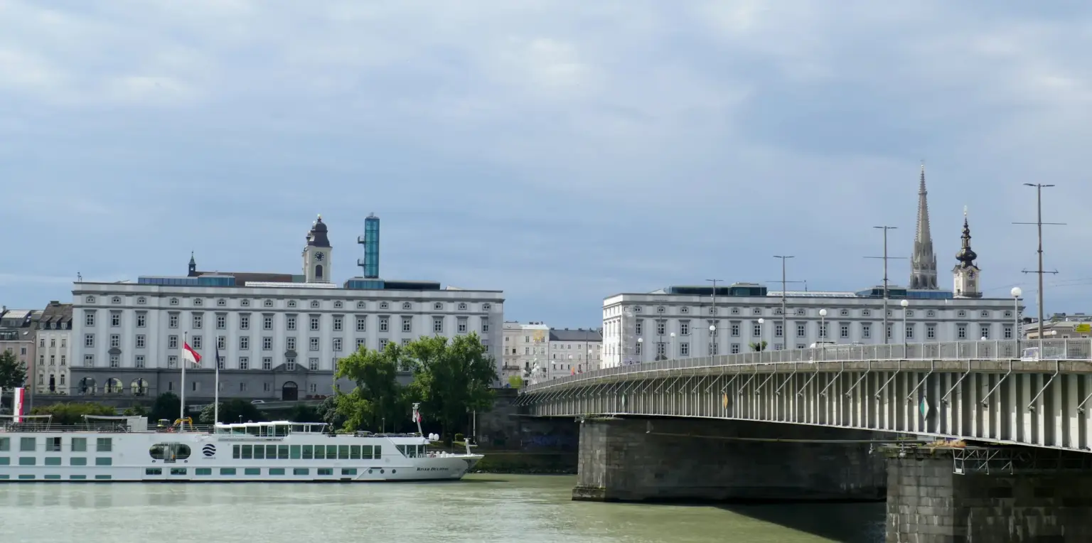 Blick über die Donau auf die beiden Brückenkopfgebäude am Linzer Hauptplatz und die Nibelungenbrücke, davor ein Ausflugsschiff